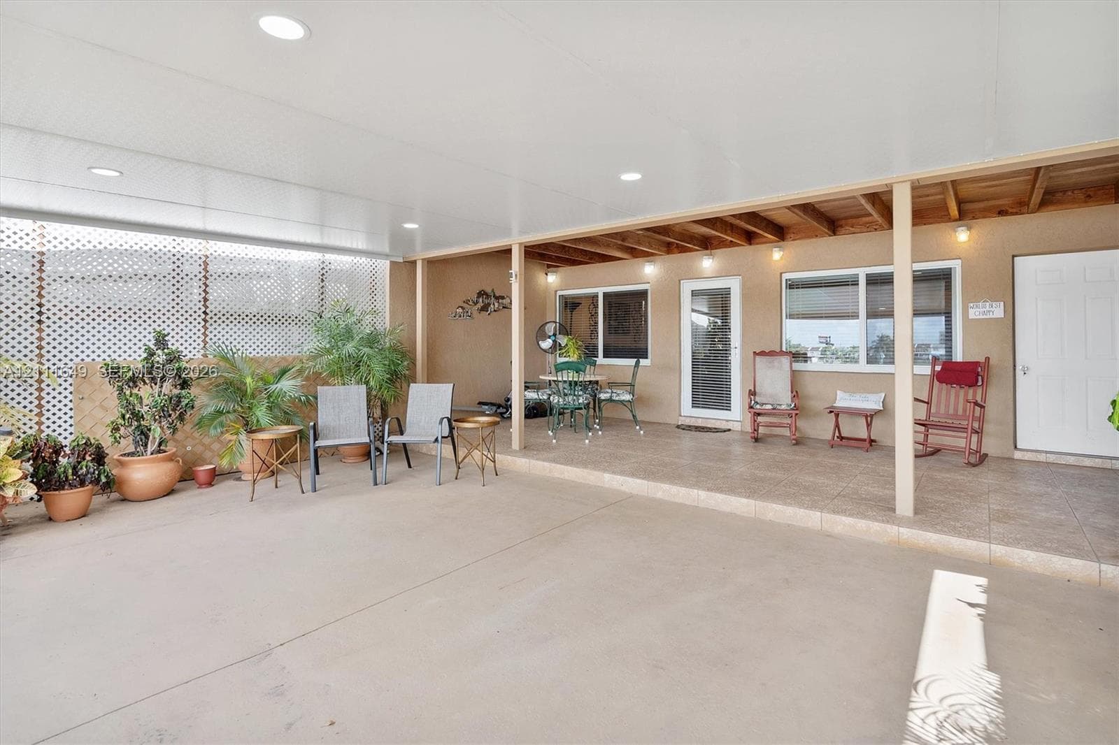 Covered outdoor patio featuring a concrete floor, recessed lighting, exposed wood ceiling beams, and white lattice privacy screening