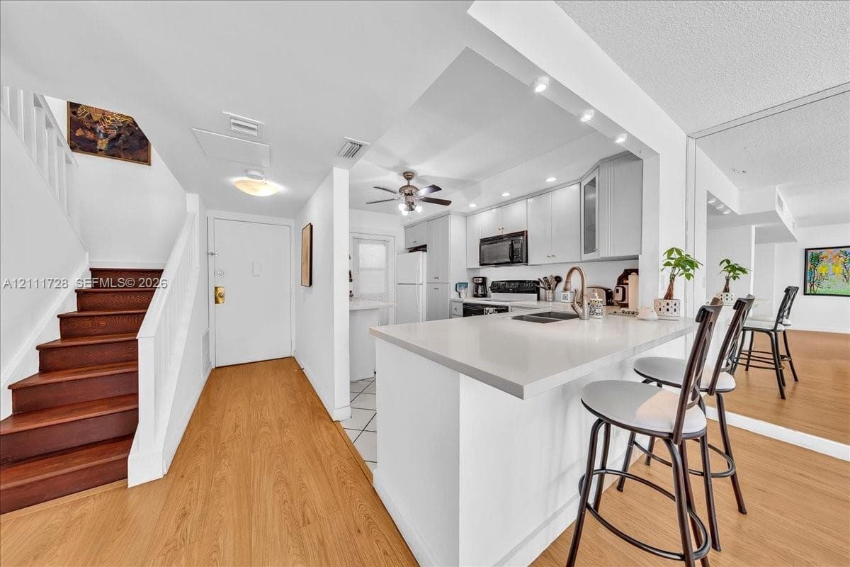 Kitchen featuring light-toned cabinetry, a quartz countertop island, wood-finish flooring, and a staircase with stained wood treads