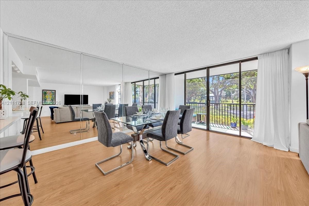 Open-concept living space featuring wood-finish flooring, full-wall mirrored accent, and floor-to-ceiling sliding glass doors opening to a balcony