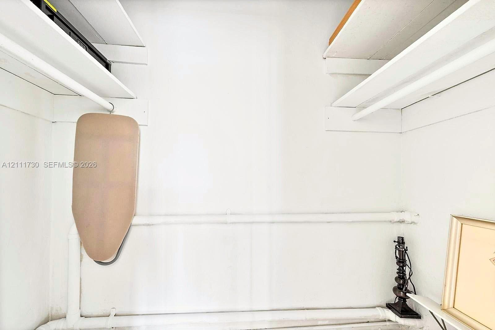 Storage closet featuring tiered white shelving and built-in white hanging rods