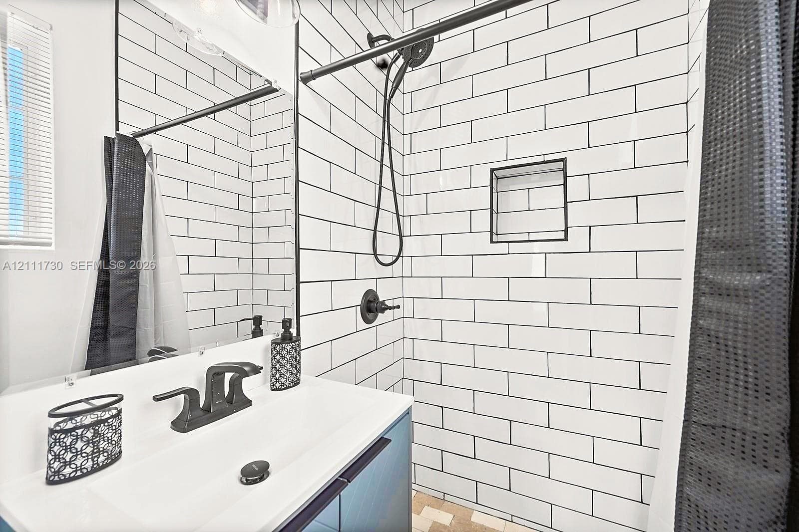 Bathroom featuring a white subway-tile shower surround with contrasting dark grout, a recessed wall niche, matte black fixtures, and a modern vanity with a rectangular basin