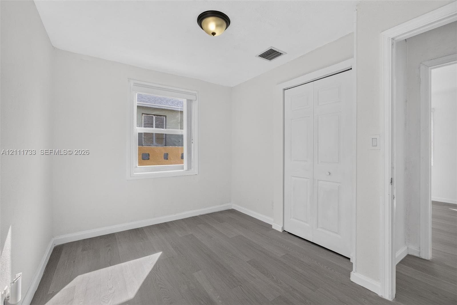 Front bedroom viewWood-finish flooring, neutral wall tones, double-door closet, and overhead flush-mount lighting