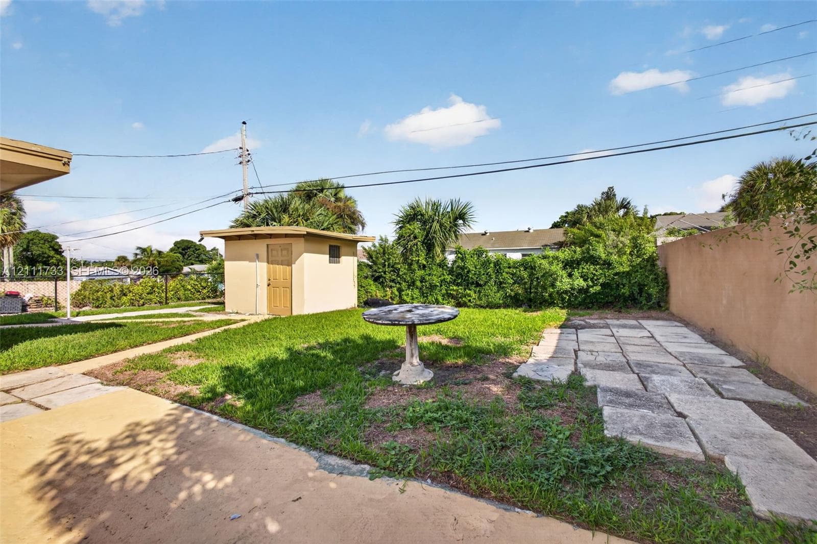 Rear outdoor space featuring a detached Shed with laundry room, concrete patio area, stone paver path, and perimeter masonry wall
