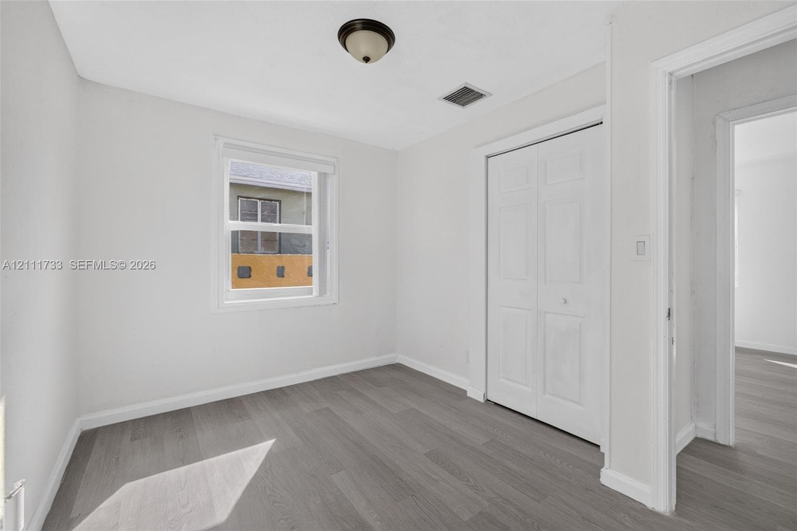 Neutral-toned room featuring grey wood-finish flooring, double-panel closet doors, and a single-hung window with a white frame