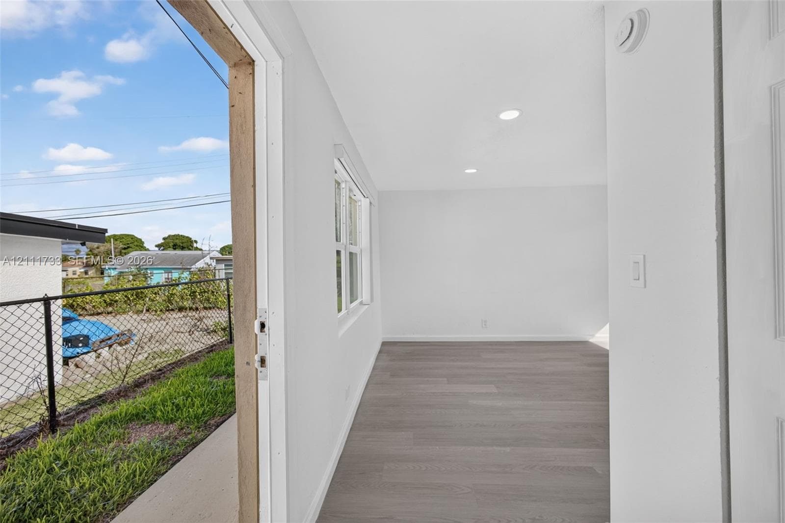 Interior view from front  area thru door (lock-off) to rear bedroom and showing open rear exterior entry door to left. featuring wood-finish flooring, recessed lighting, and a multi-pane window
