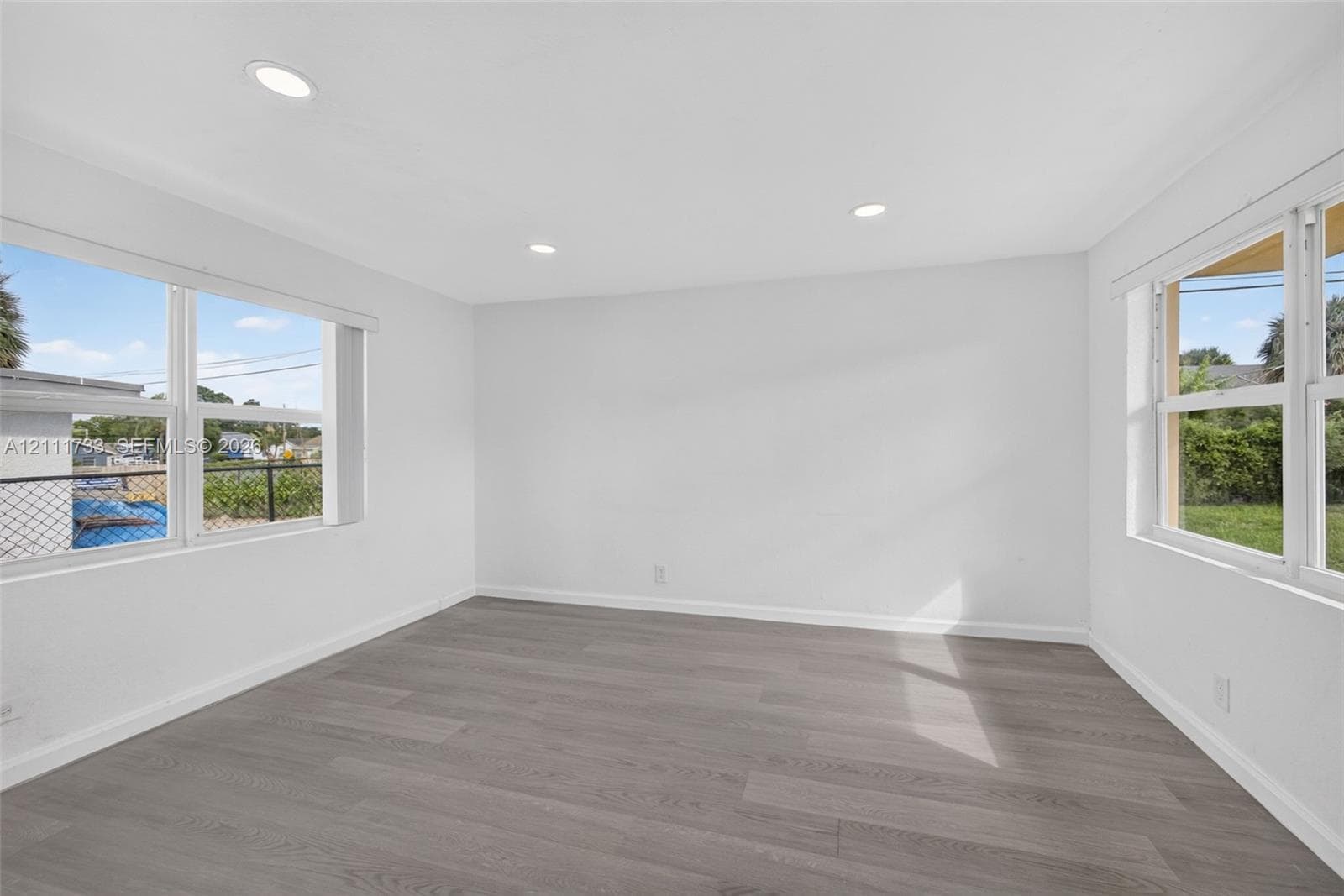 Rear bedroom features Neutral-toned wood-finish flooring, recessed lighting, and multiple large windows with white trim