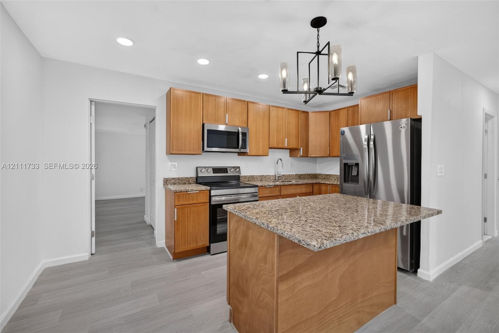 Kitchen featuring natural wood cabinetry, stone-surface countertops, stainless steel appliances, a central island, and a modern geometric pendant light fixture