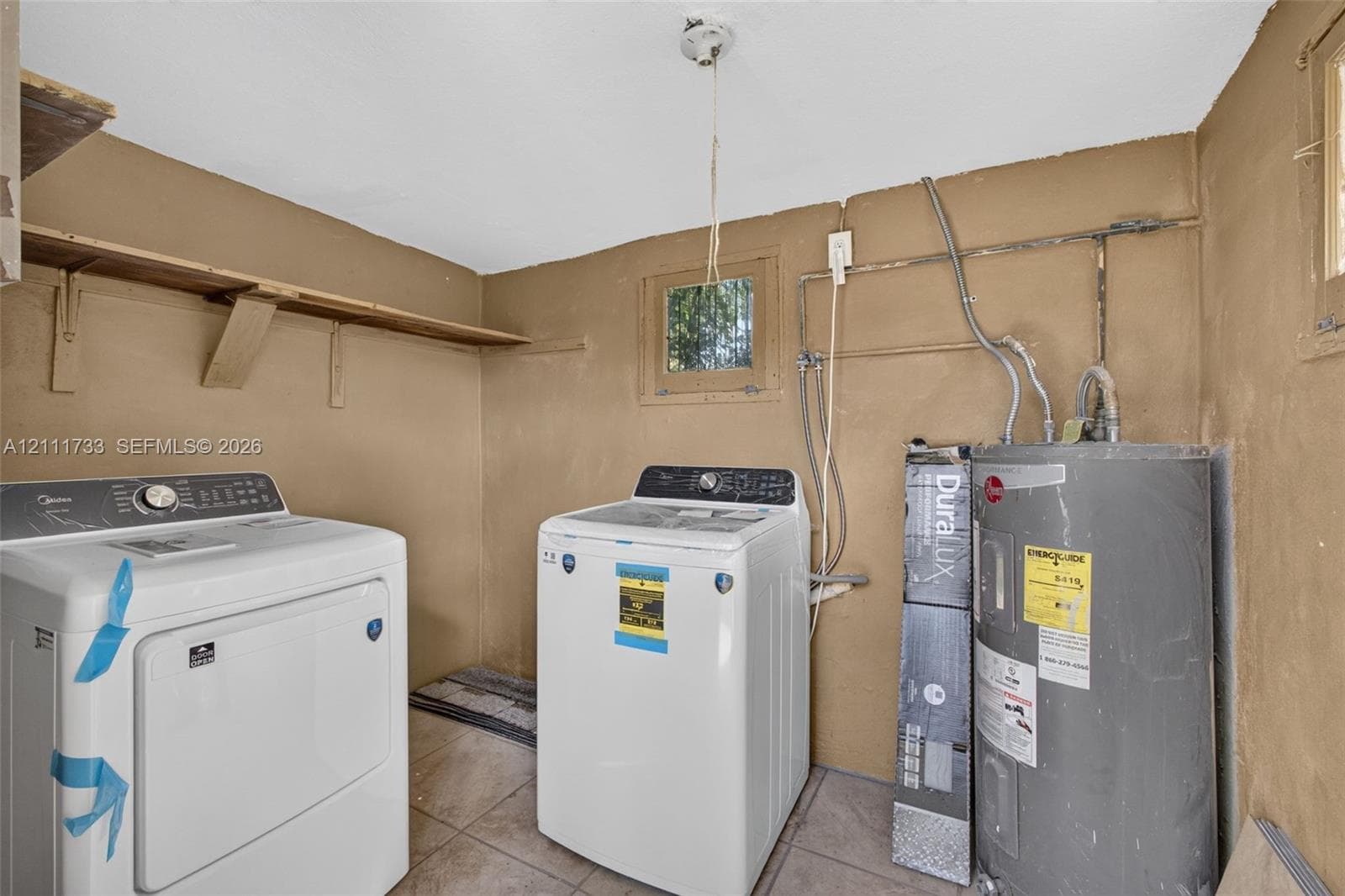 Interior of out Building featuring brand new Washer & Dryer, built-in wooden shelving, tile flooring, window, and and electric water heater.