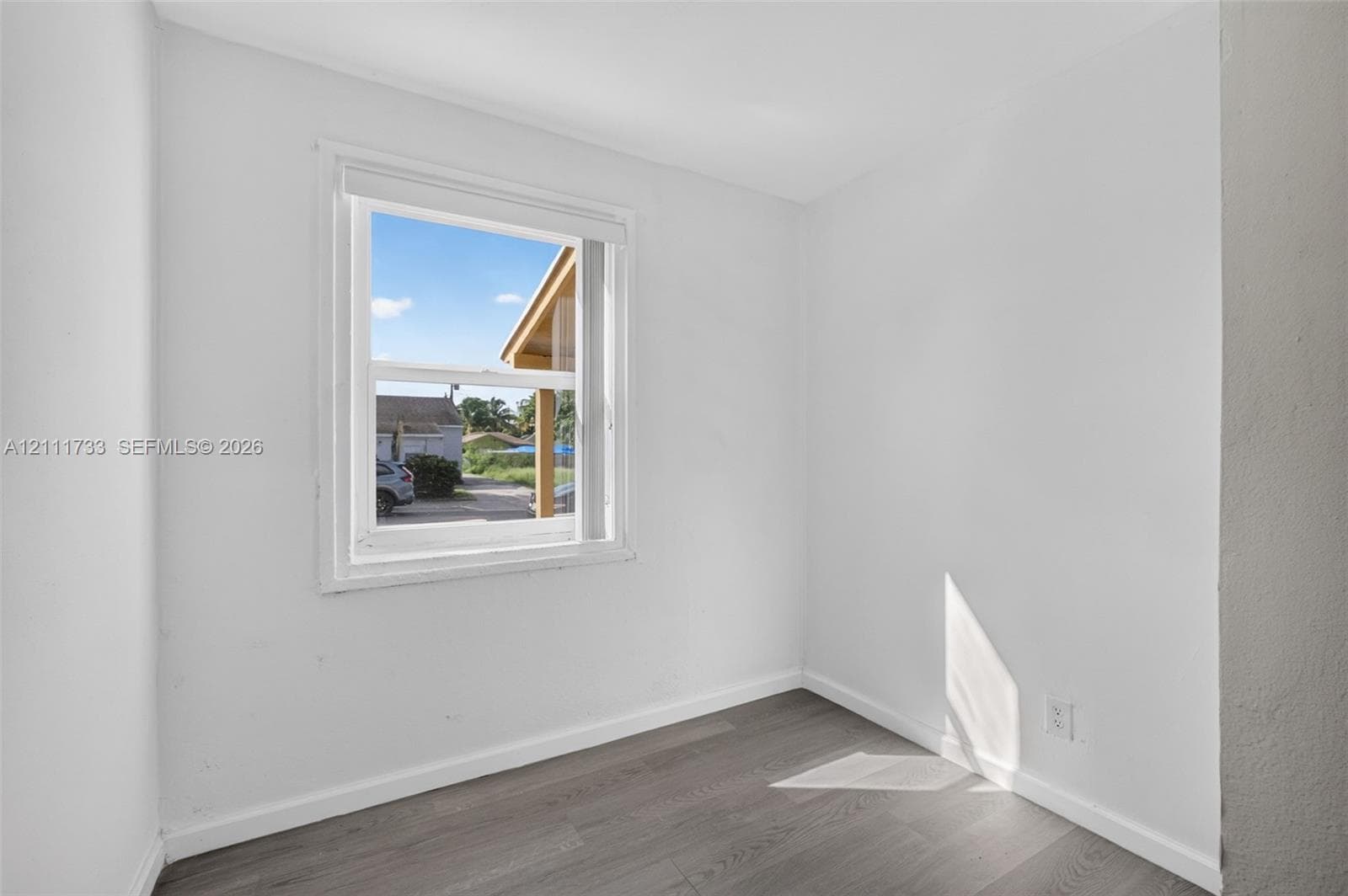 Front bedroom featuring white-painted walls and wood-finish flooring with an inset double-hung window