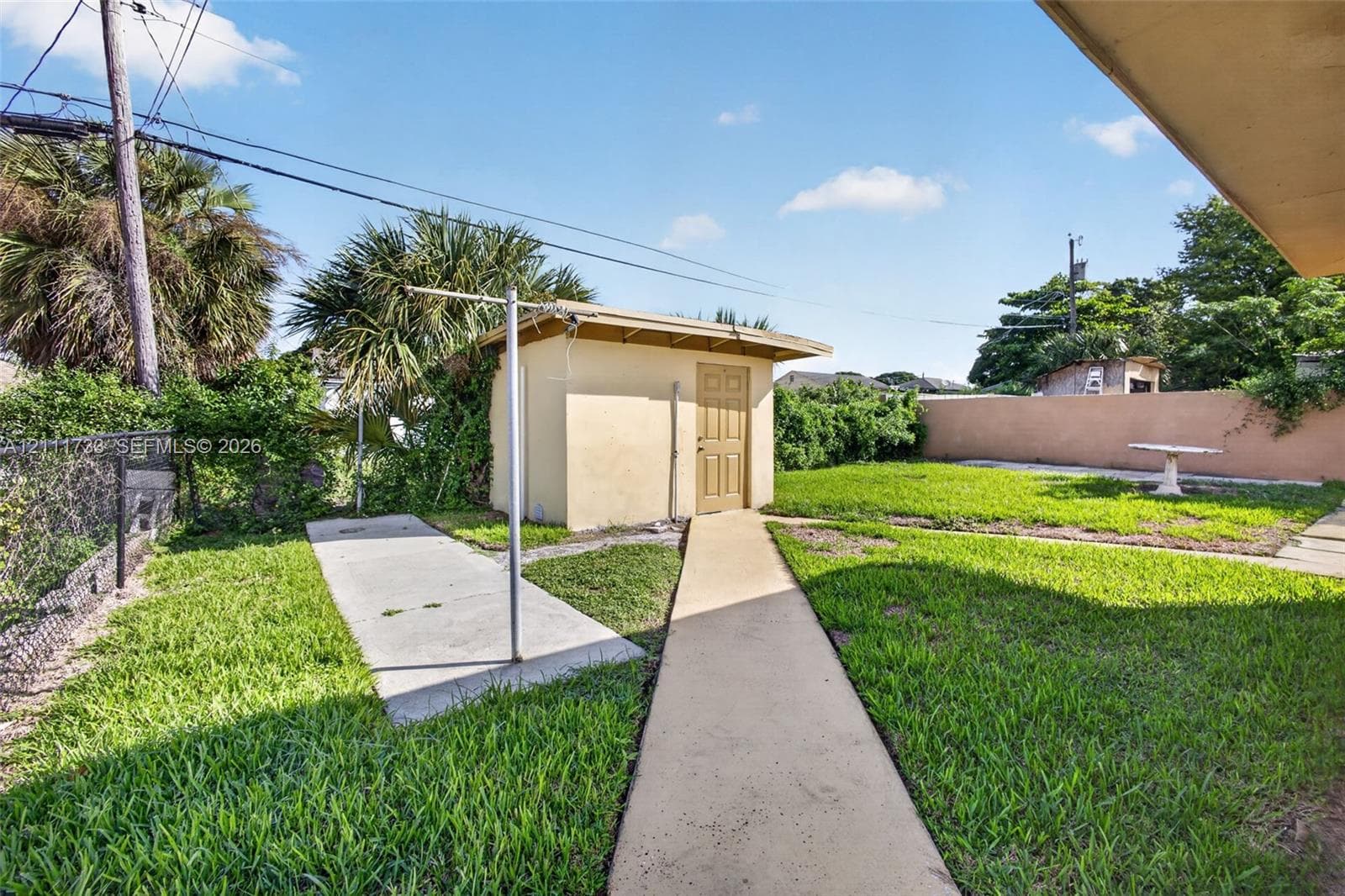 Rear yard from left side of home, featuring a detached shed with  laundry room, concrete pathways, perimeter masonry wall.