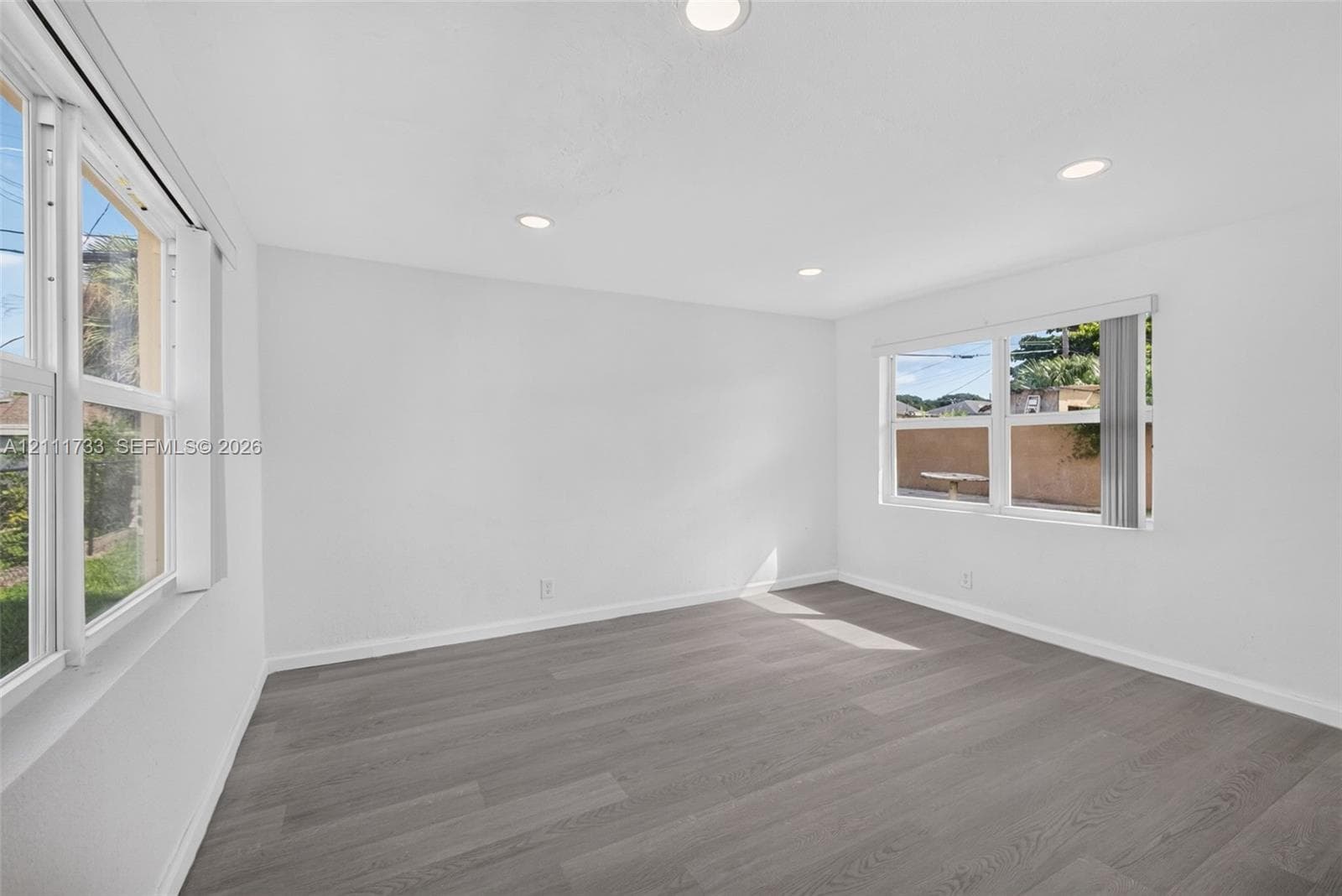 Interior features of Rear bedroom wood-finish flooring, recessed lighting, and dual impact windows with horizontal blinds.