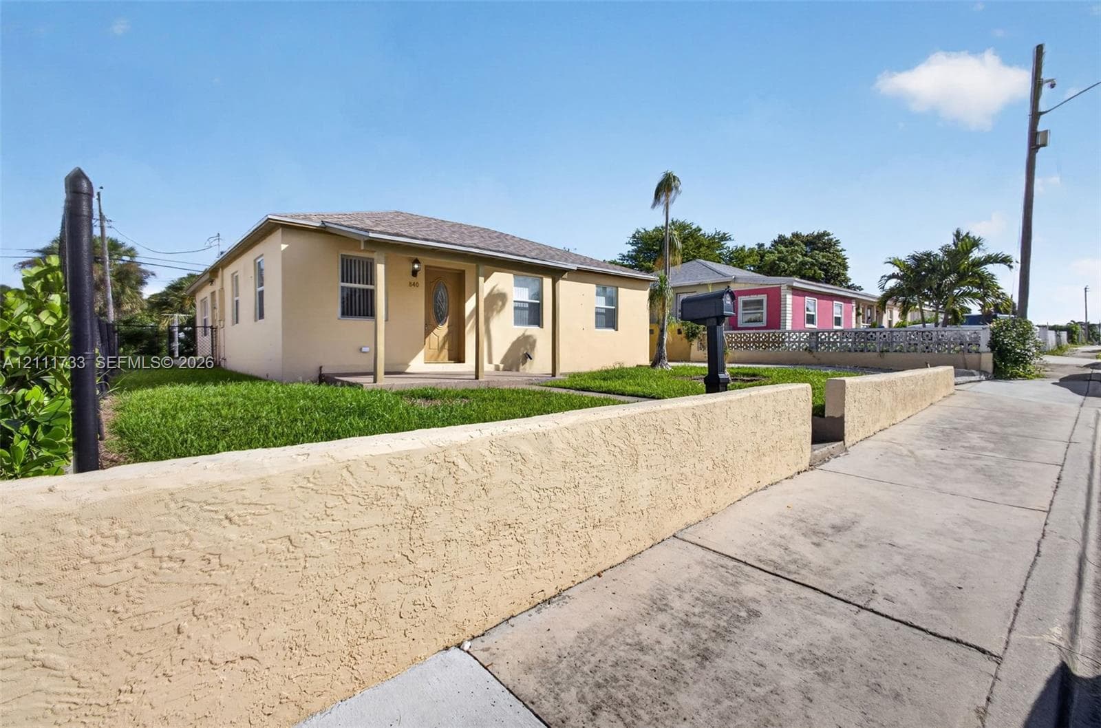 Single-story stucco exterior featuring a covered front porch, low-profile masonry perimeter wall, and manicured lawn