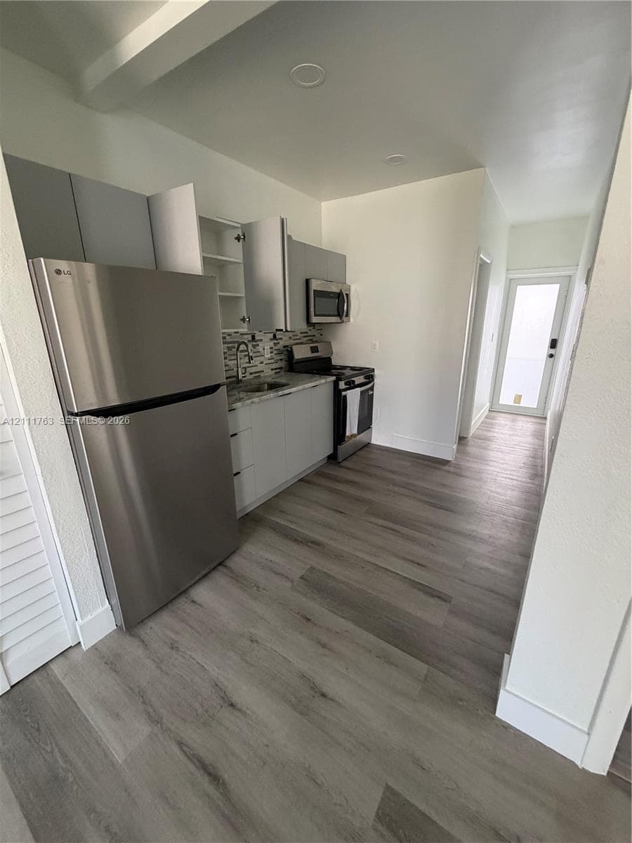 Kitchen featuring wood-finish flooring, stainless steel appliances, flat-panel cabinetry, a multi-tonal tile backsplash, and recessed lighting