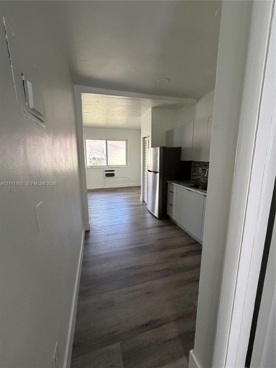 Kitchen featuring white cabinetry, wood-finish flooring, a stainless steel refrigerator, and a tiled backsplash