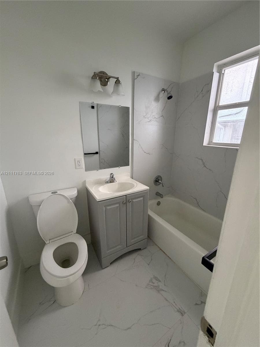 Bathroom featuring a vanity with a white composite countertop, large-format stone-patterned tile flooring, full-height stone-patterned tile shower surround, and a wall-mounted light fixture