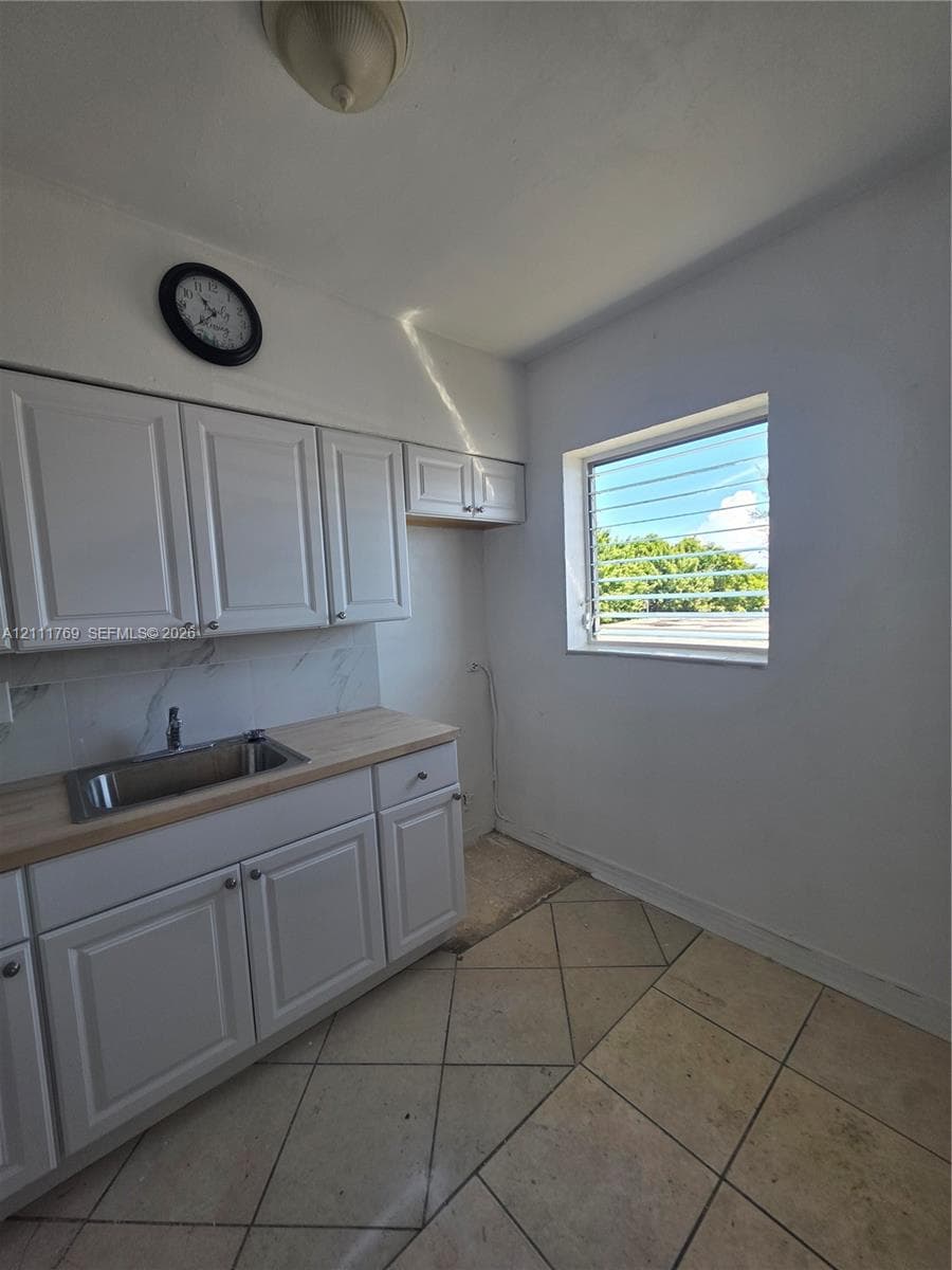 White shaker-style cabinetry, stainless steel sink, wood-finish countertop, tiled backsplash, and diagonal tile flooring