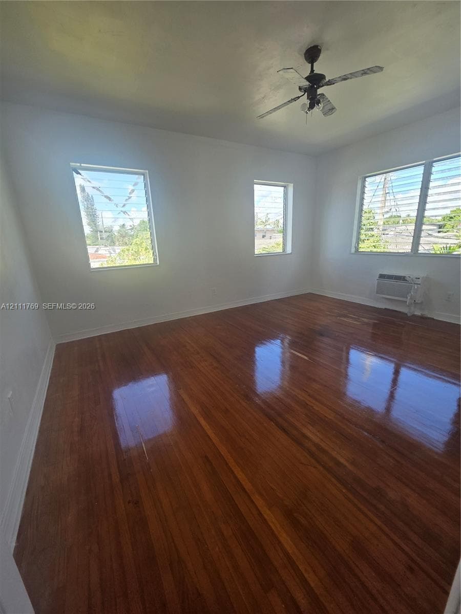 Room featuring wood-finish flooring, white walls, multiple louvered windows, and a ceiling fan