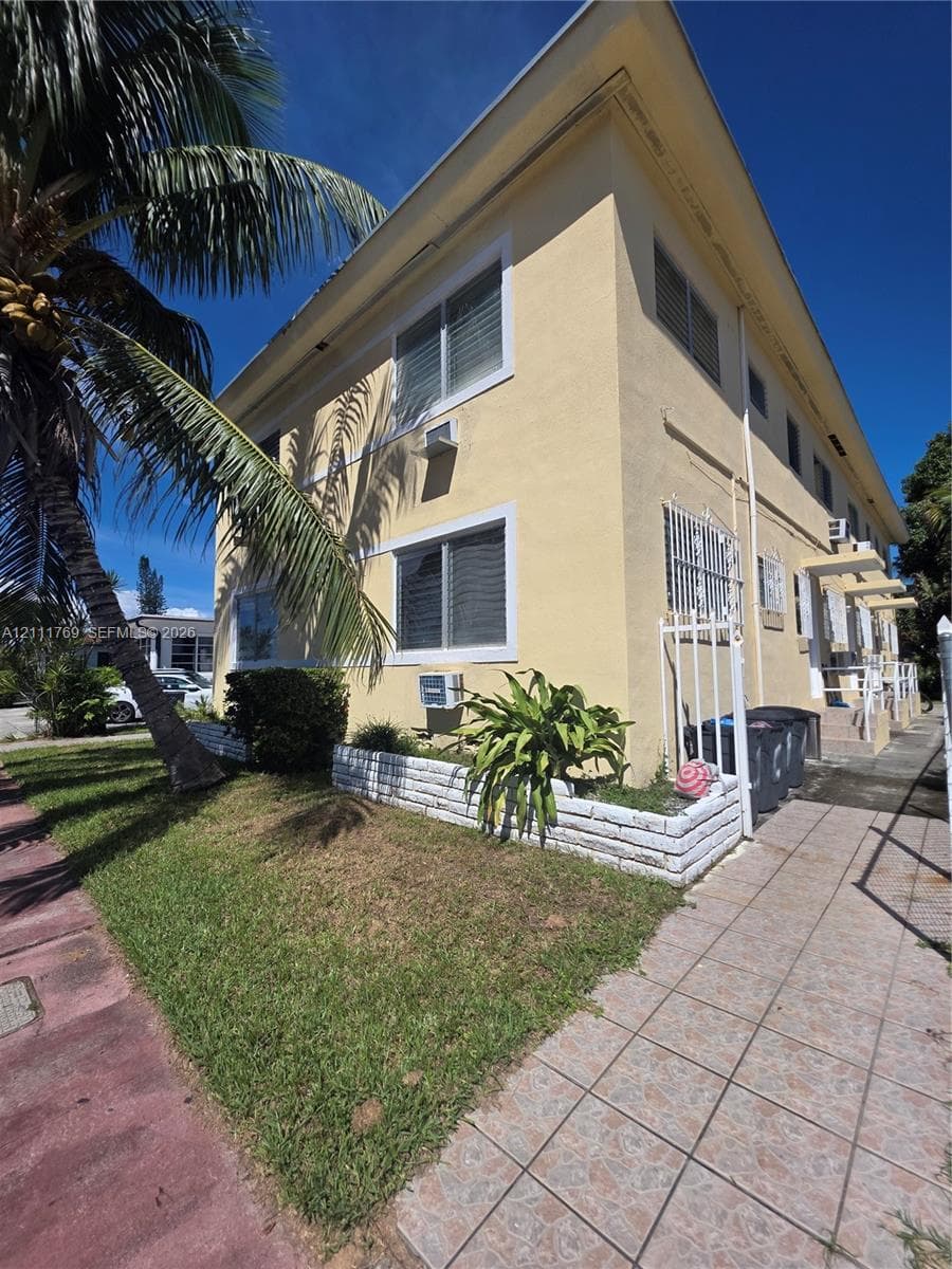 Two-story stucco exterior featuring horizontal windows, a paved walkway, and a manicured raised planter bed