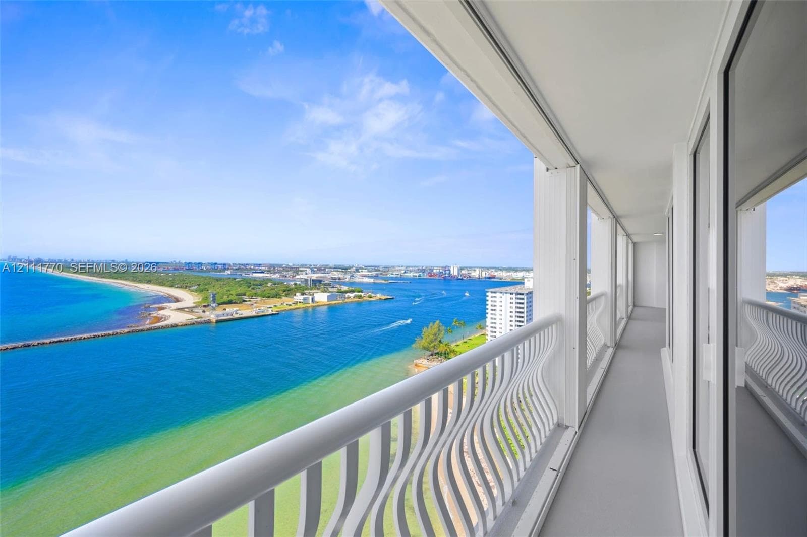 High-rise balcony featuring a white metal serpentine railing, neutral flooring, and expansive water frontage