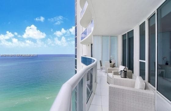 Expansive curved balcony featuring floor-to-ceiling glass railings, large-format tile flooring, and full-height glass sliding door access