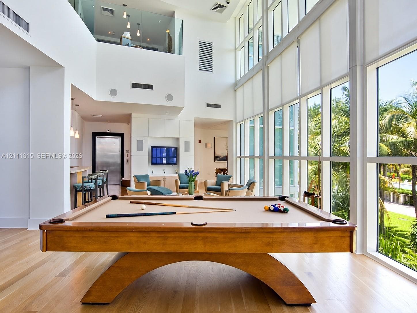 Double-height ceiling, floor-to-ceiling windows, wood-finish flooring, built-in wet bar, and glass-paneled mezzanine railing
