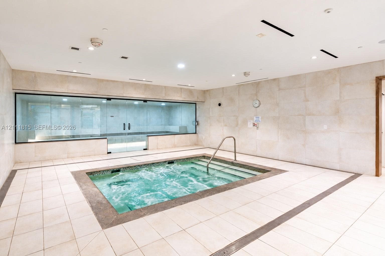 Indoor spa room featuring a tiled plunge pool, recessed lighting, expansive wall-to-wall glass enclosure, and stone-finish wall cladding
