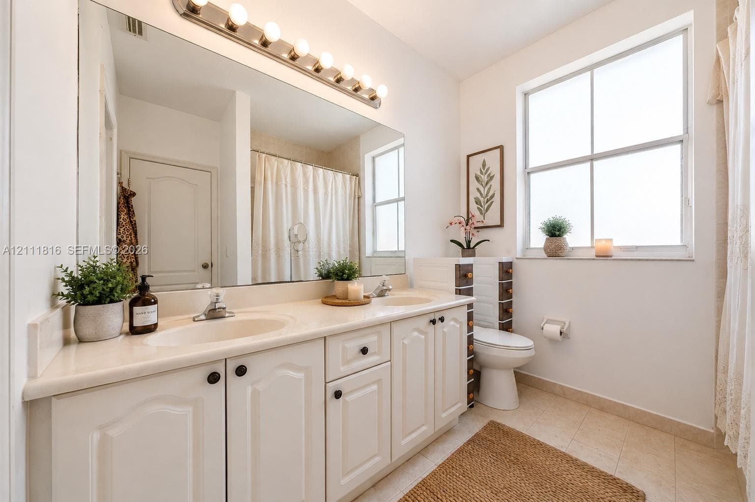 Double vanity with integrated sinks, neutral solid-surface countertop, full-width mirror, multi-bulb wall lighting, and porcelain tile flooring