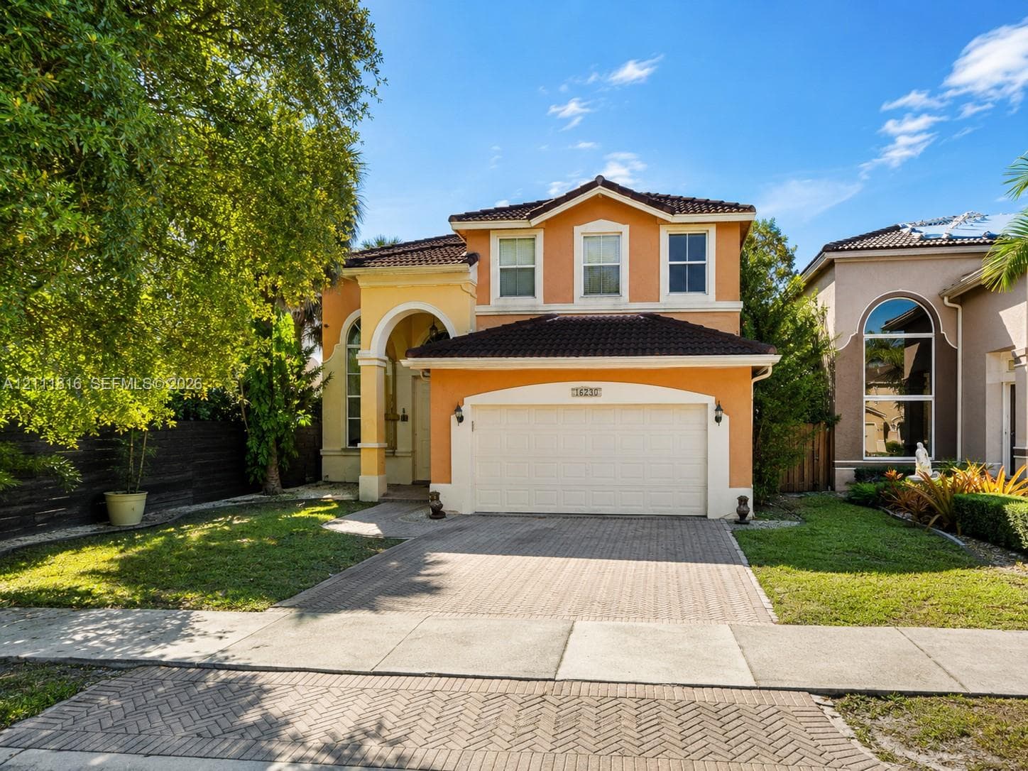 Two-story stucco exterior featuring an arched entryway, a multi-gabled roofline with dark tile shingles, and a paver driveway