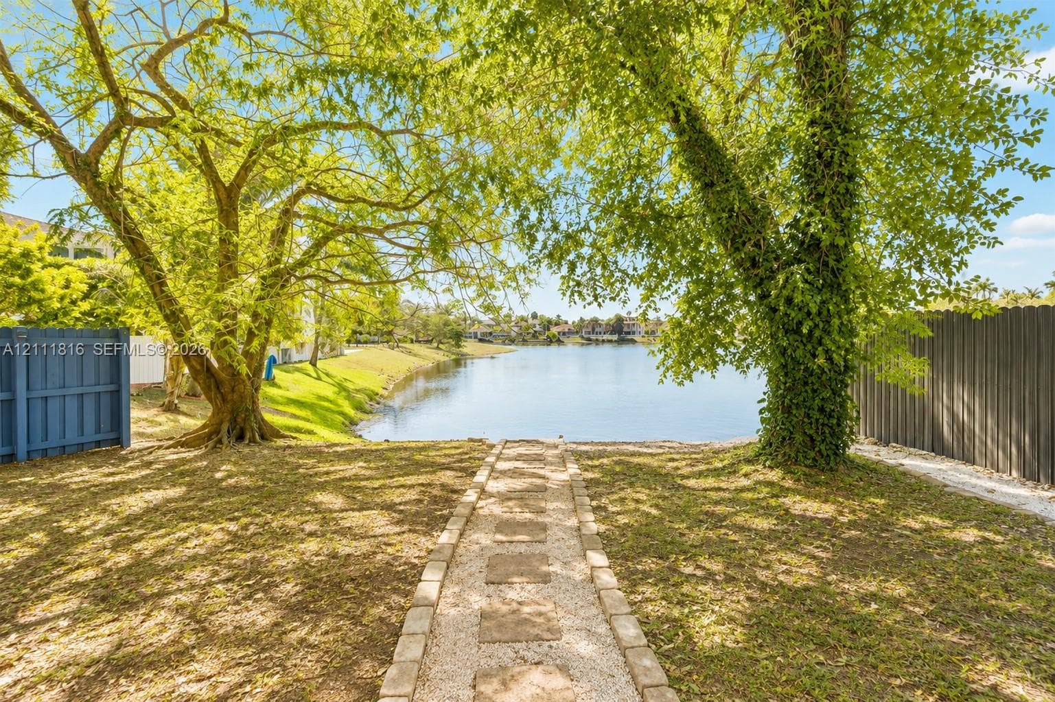 Waterfront lot featuring a stone-paver walkway, mature trees, and privacy fencing