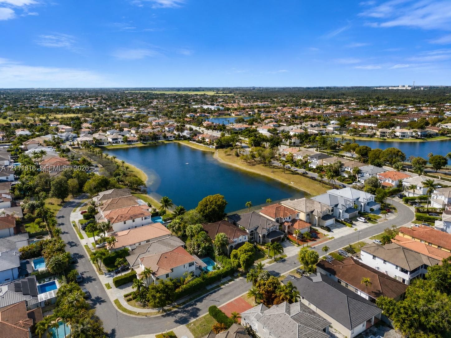 Aerial view of residential properties featuring tile roofing, paved streets, and a central community lake