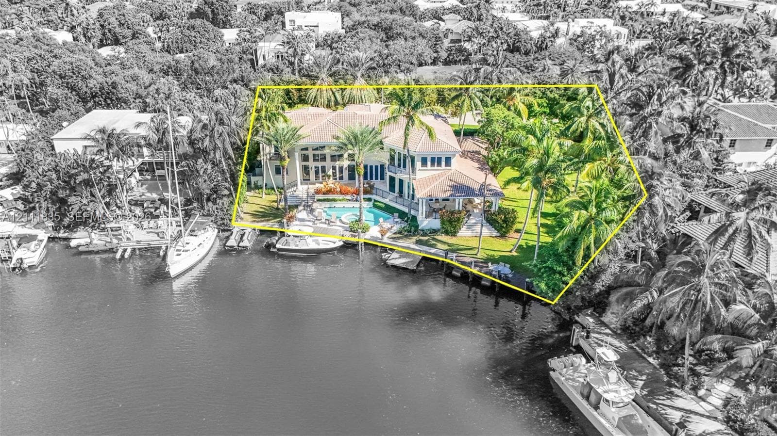 Waterfront estate featuring a multi-story residence, private swimming pool with integrated spa, mature palm landscaping, and deep-water dockage