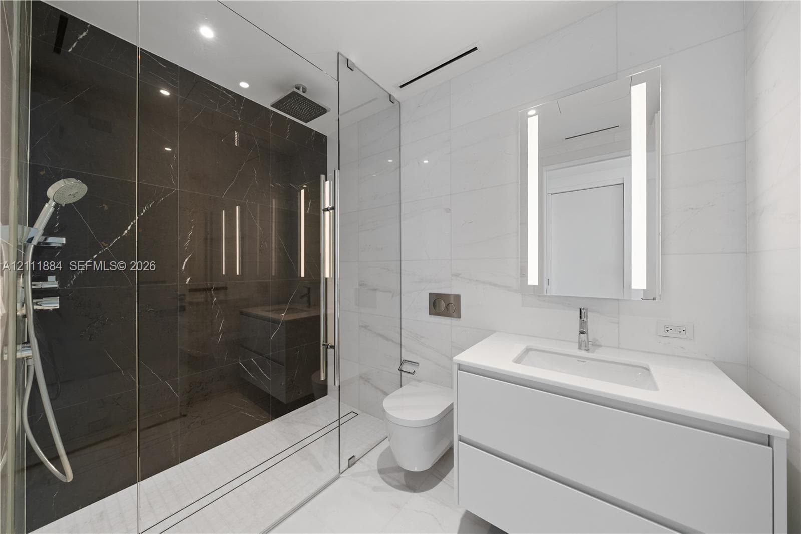 Bathroom featuring a walk-in shower with dark tile surround, a wall-mounted toilet, a floating vanity with a stone countertop, and an integrated LED mirror