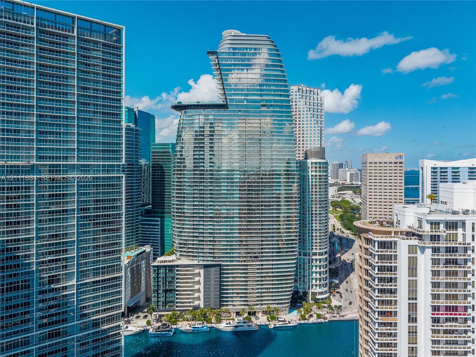 High-rise glass facade building featuring a curved architectural profile, multiple cantilevered terraces, and deep-water boat slips