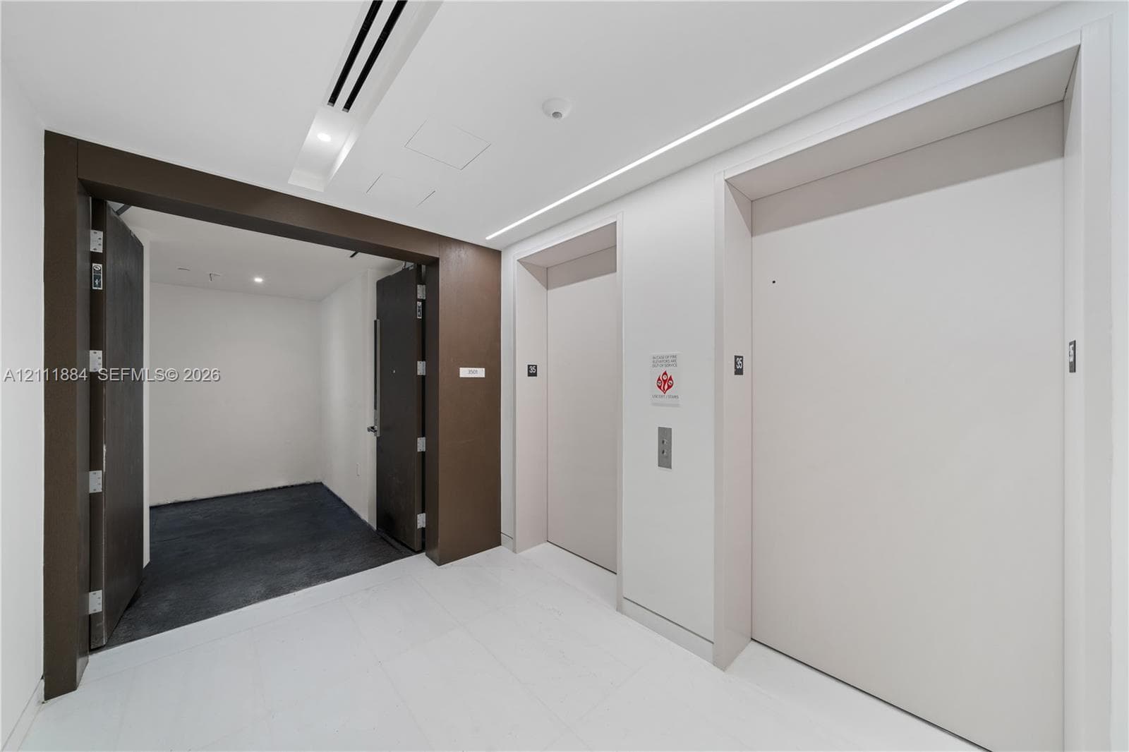 Elevator landing featuring dual elevator doors, stone flooring, recessed ceiling lighting, and a dark wood-finish entryway frame