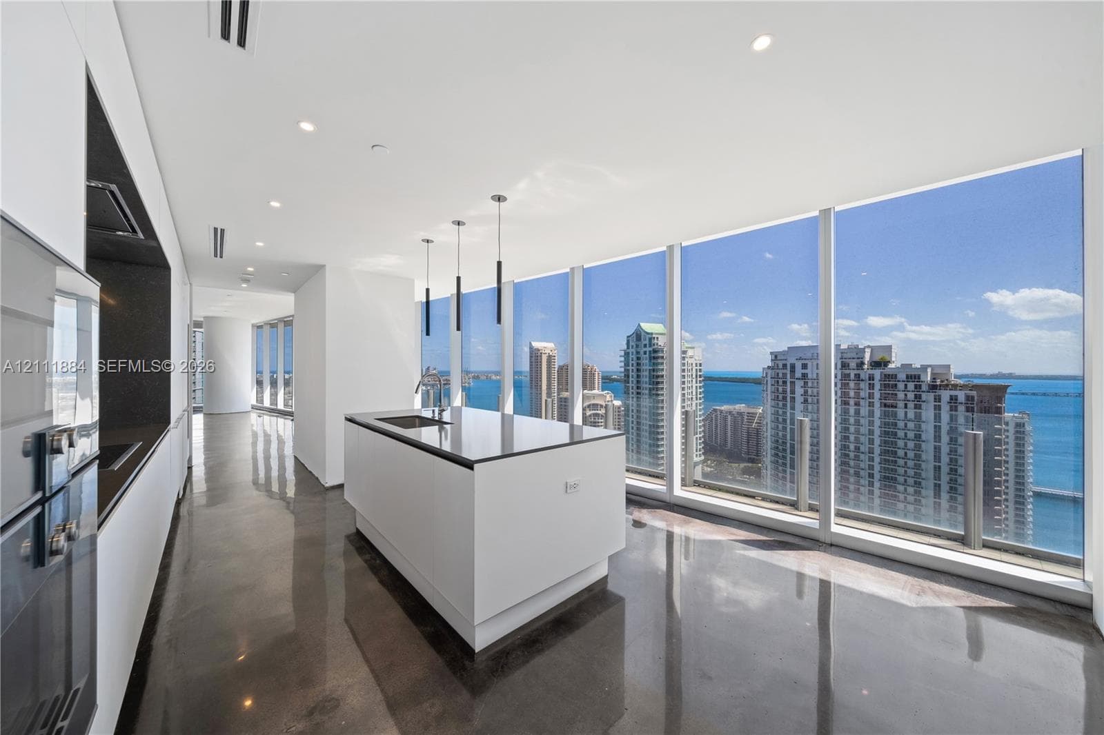 Modern kitchen featuring floor-to-ceiling windows, polished concrete flooring, a central island with a stone-surfaced countertop, integrated cabinetry, and recessed lighting