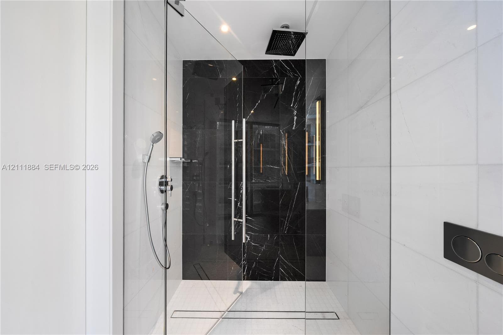 Walk-in shower featuring glass enclosure, ceiling-mounted rainfall showerhead, handheld shower fixture, black stone-finish tile accent wall, and linear floor drain