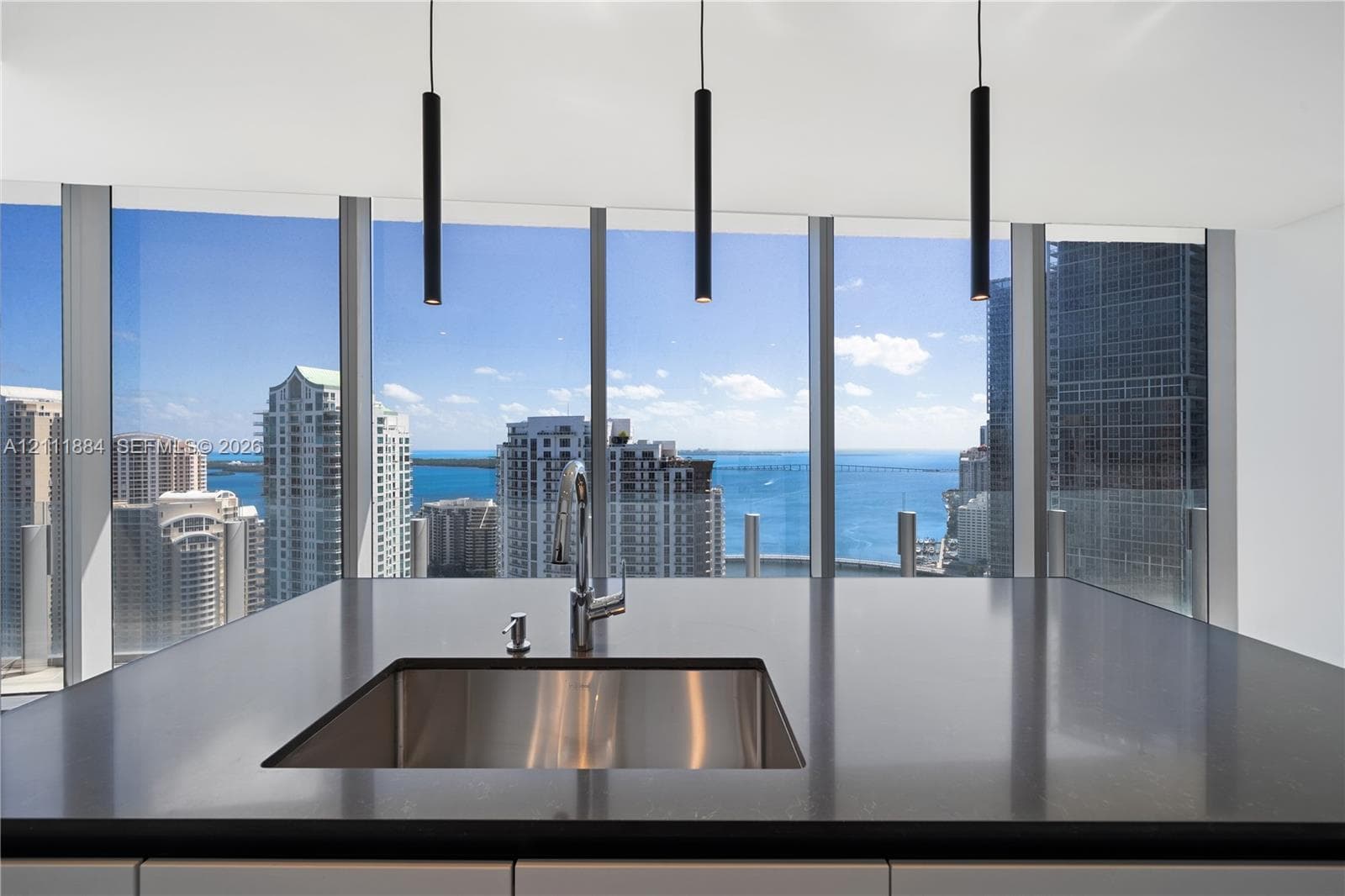 Kitchen island featuring dark solid-surface countertops, an undermount stainless steel sink with a high-arch faucet, floor-to-ceiling windows, and matte black cylindrical pendant lighting