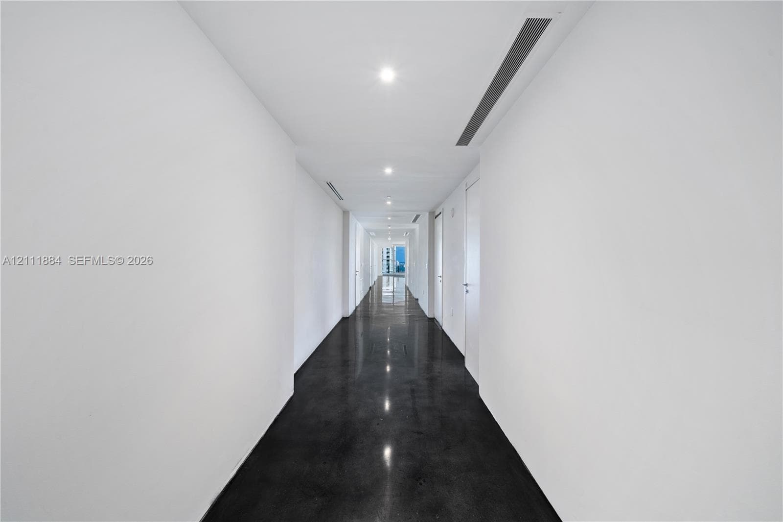 Hallway featuring high-gloss concrete flooring, recessed ceiling lighting, and crisp white wall finishes