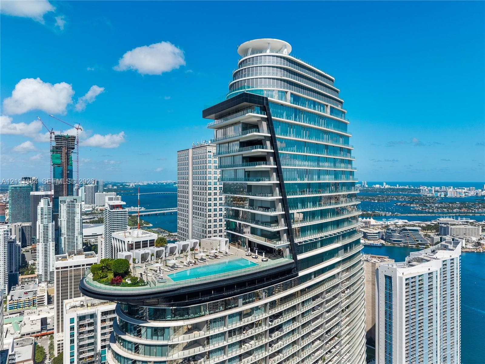 High-rise structure featuring floor-to-ceiling glass paneling, cantilevered balconies, a rooftop pool, and extensive exterior deck space