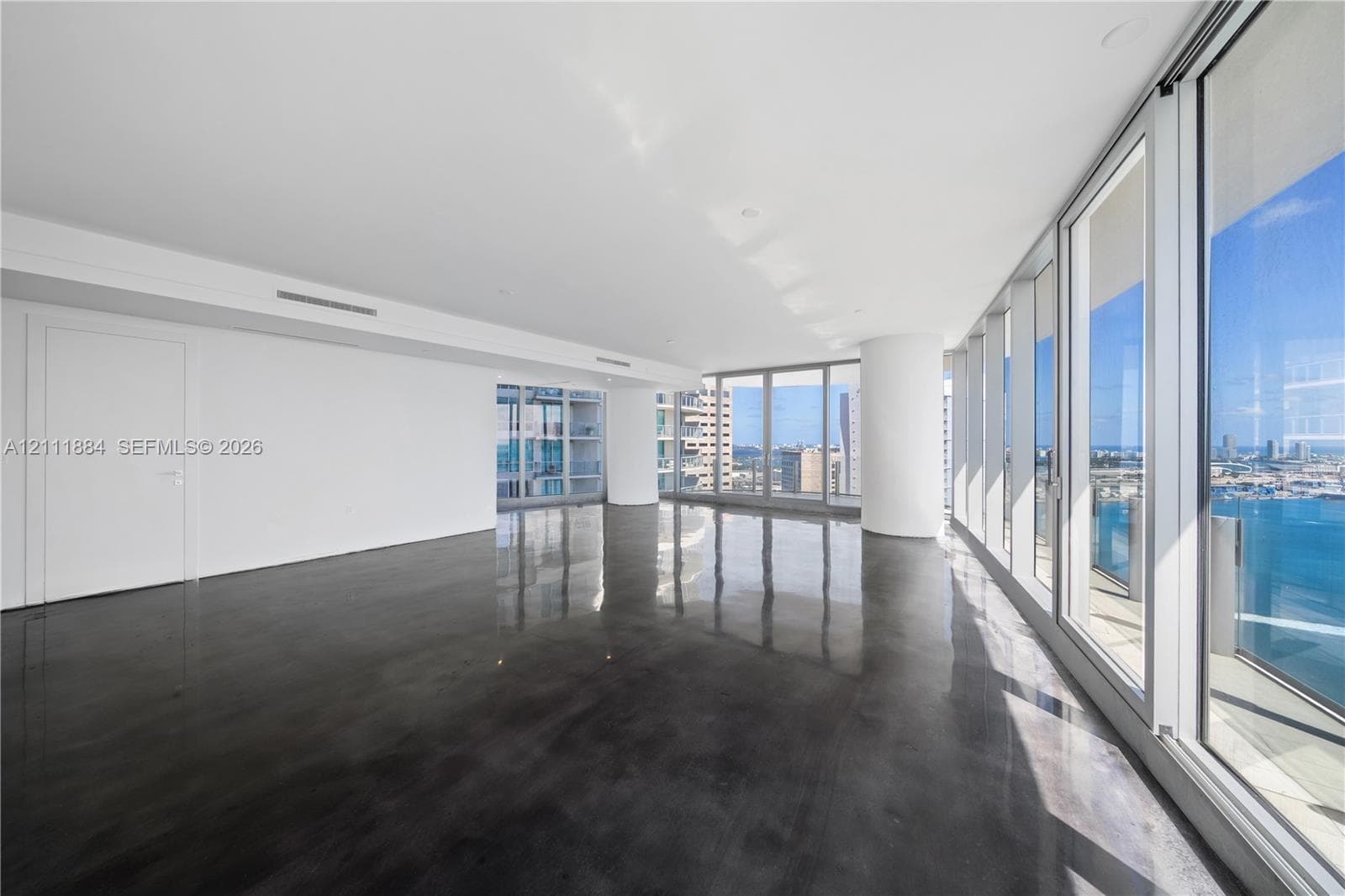 Expansive interior space featuring high-gloss polished concrete flooring, floor-to-ceiling glass panel walls, and cylindrical architectural columns