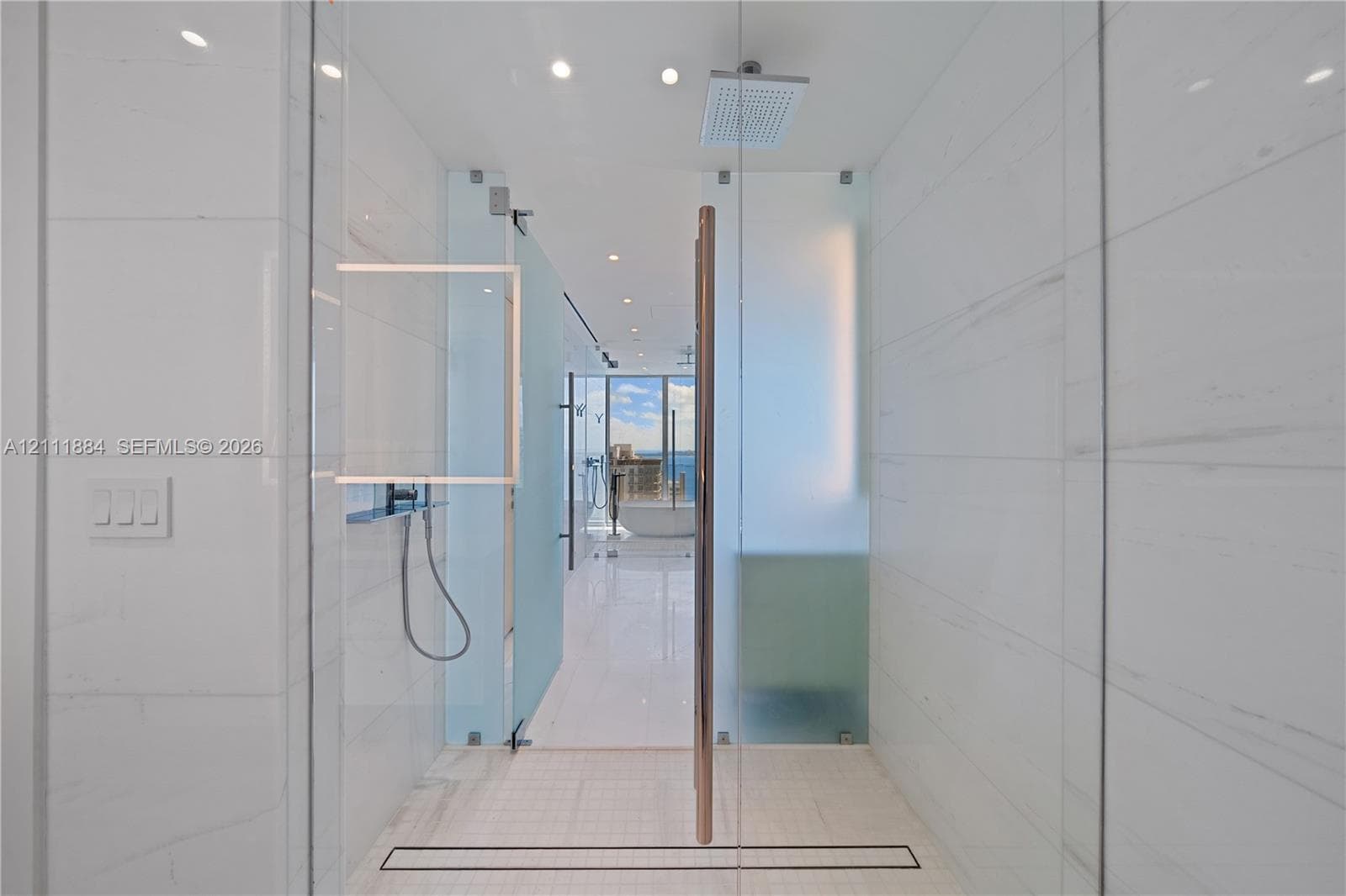 Walk-in shower featuring floor-to-ceiling tiled walls, frameless glass door, ceiling-mounted rainfall showerhead, handheld shower fixture, and linear drain