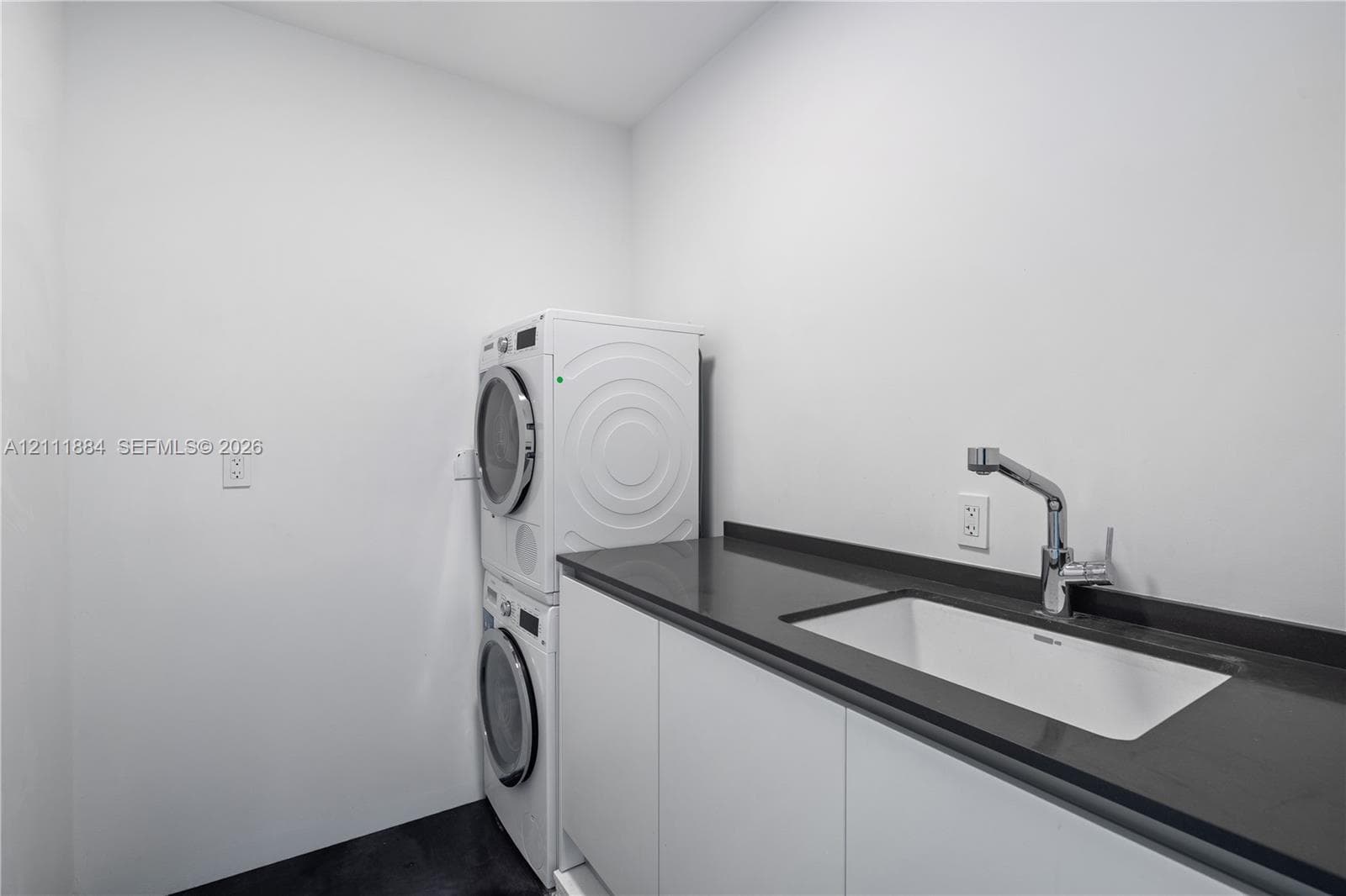 Laundry room featuring white cabinetry, a dark solid-surface countertop, an integrated rectangular basin, and a deck-mounted gooseneck faucet