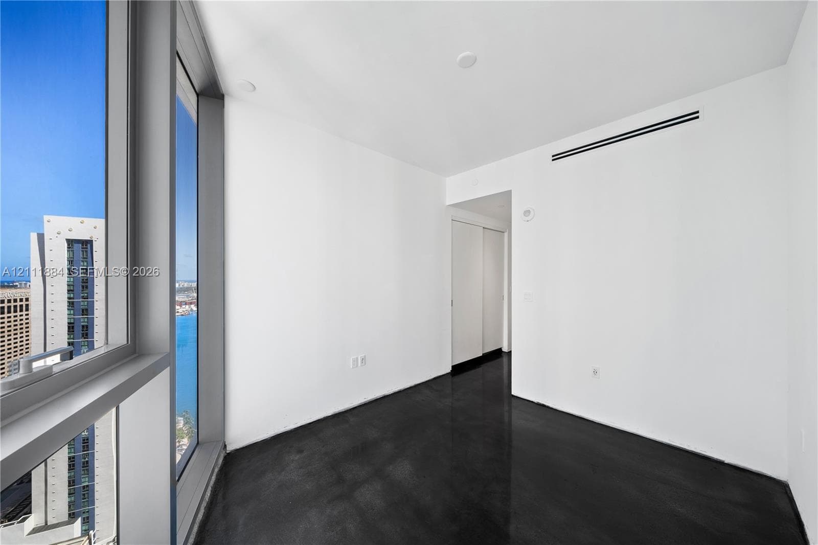 Floor-to-ceiling windows featuring urban scenery, polished concrete flooring, white walls, and interior sliding closet doors