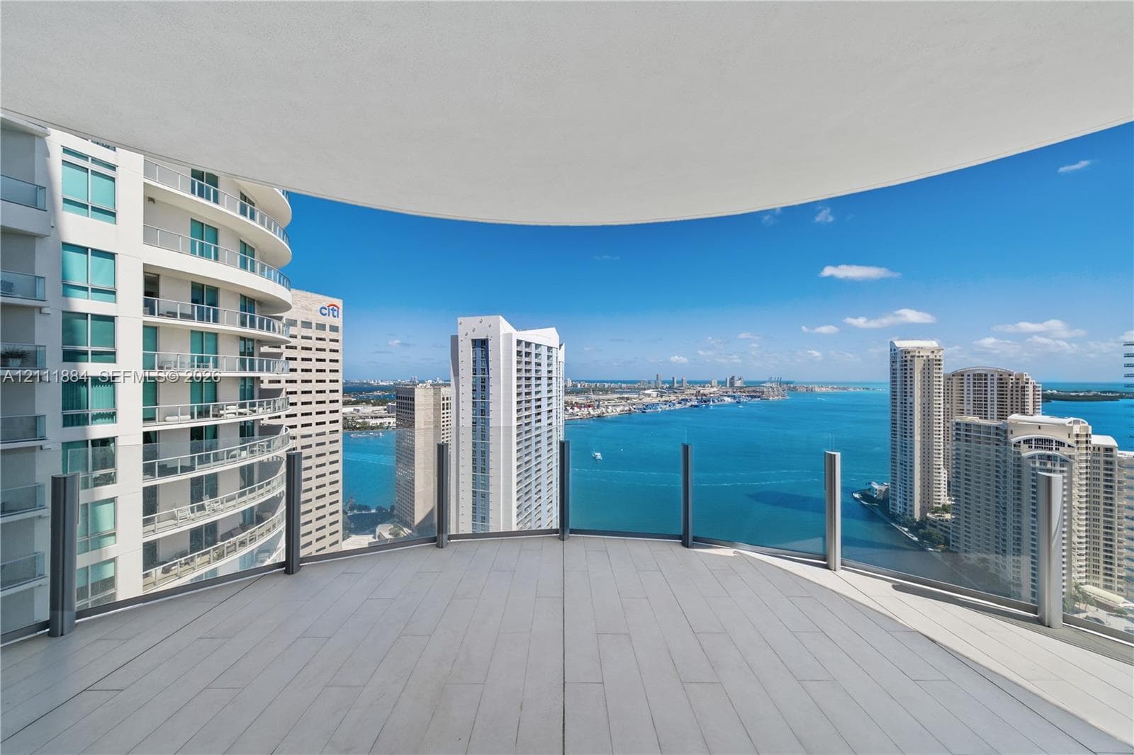 Curved expansive balcony featuring wood-finish flooring and floor-to-ceiling glass panel railings