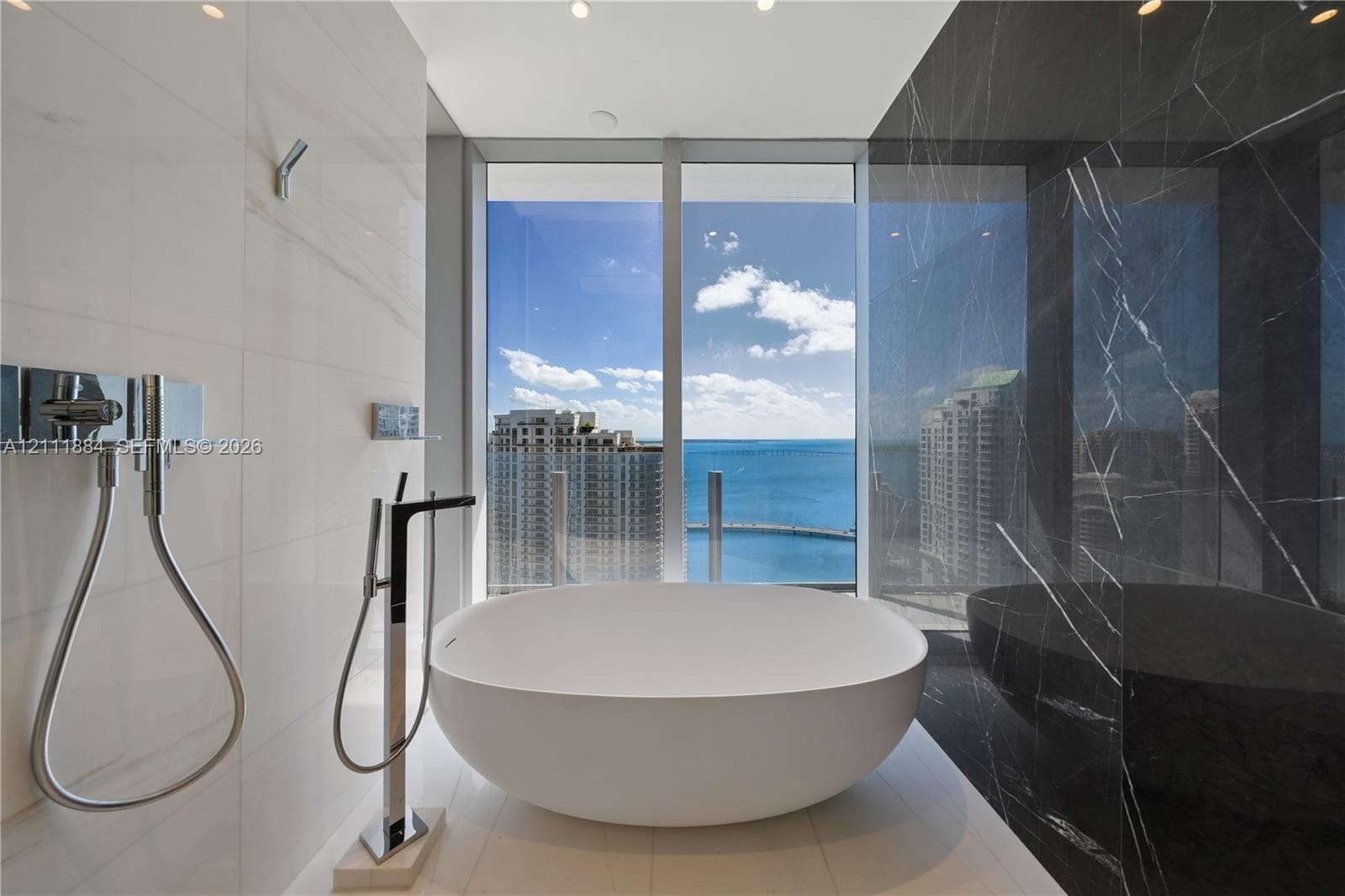 Freestanding soaking tub, floor-to-ceiling windows, high-contrast wall tiling, polished chrome fixtures, and open water scenery