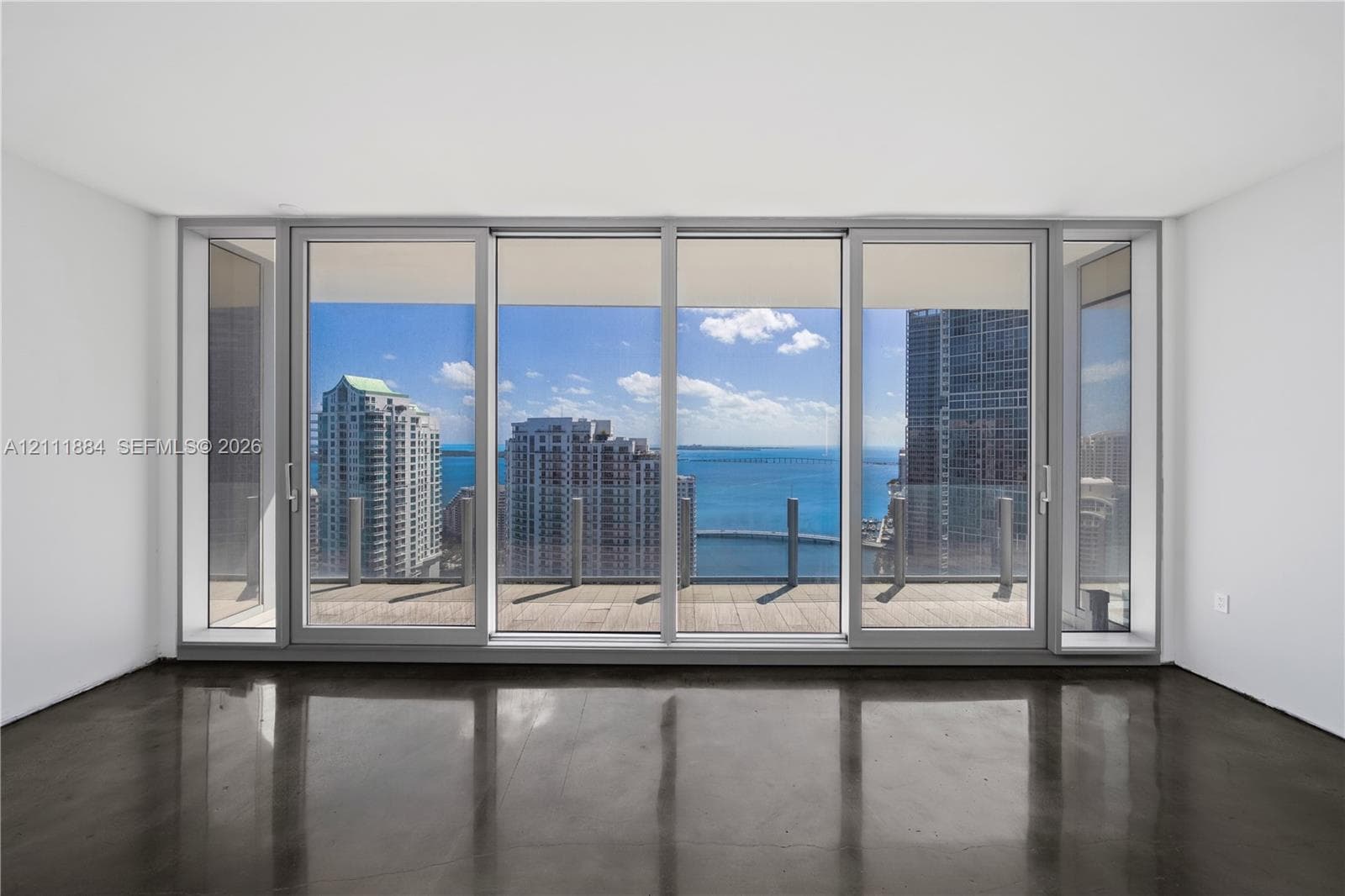 Floor-to-ceiling sliding glass panels, polished concrete flooring, and an expansive outdoor terrace featuring a glass railing with water and city skyline vistas