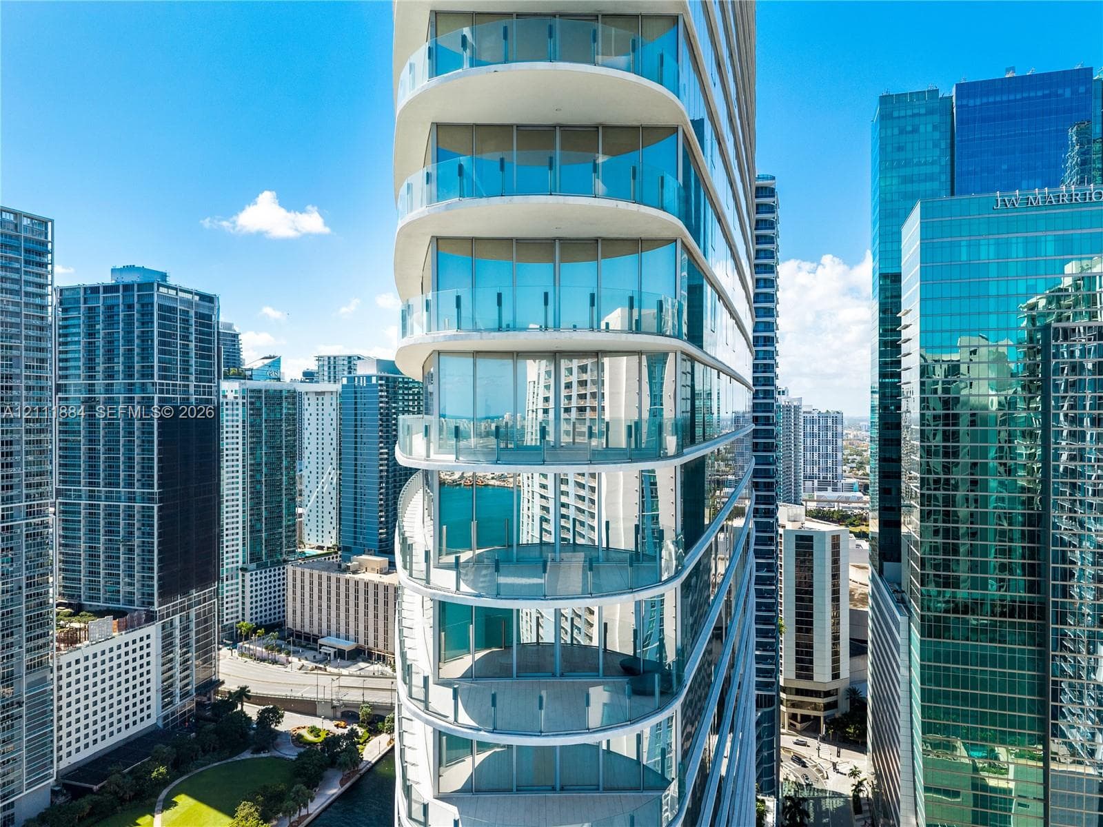 High-rise architectural exterior featuring tiered, curved structural design, floor-to-ceiling glass wall systems, and wrap-around glass panel balcony railings