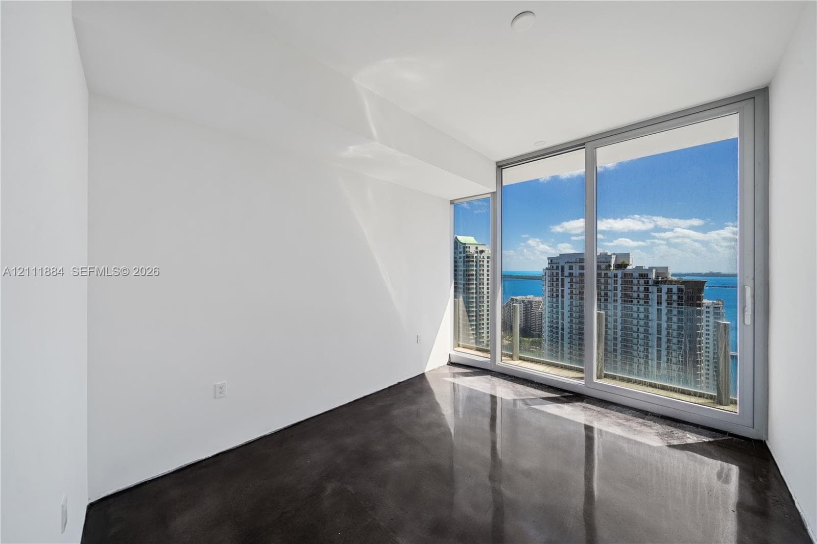 Floor-to-ceiling glass sliding doors, polished concrete flooring, and expansive water and urban skyline backdrop
