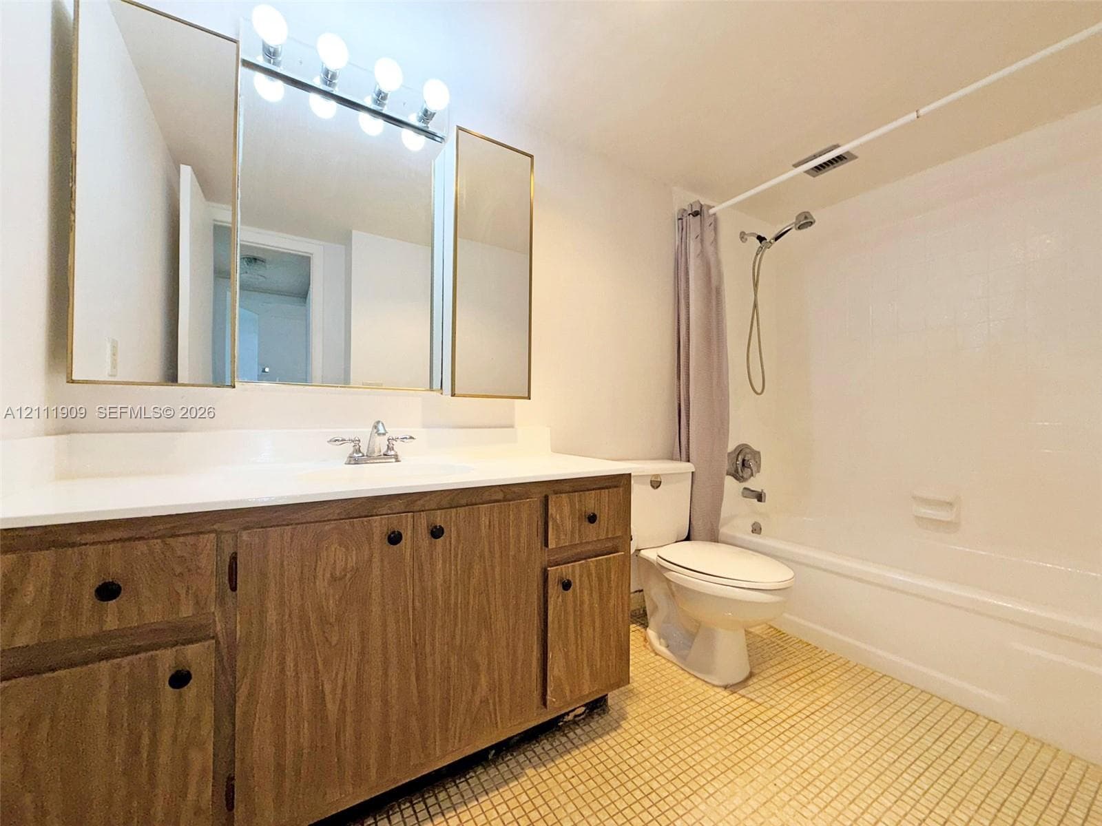 Bathroom featuring a wood-finish vanity with a white countertop, three-section mirrored medicine cabinet, integrated shower and tub enclosure, and ceramic tile flooring