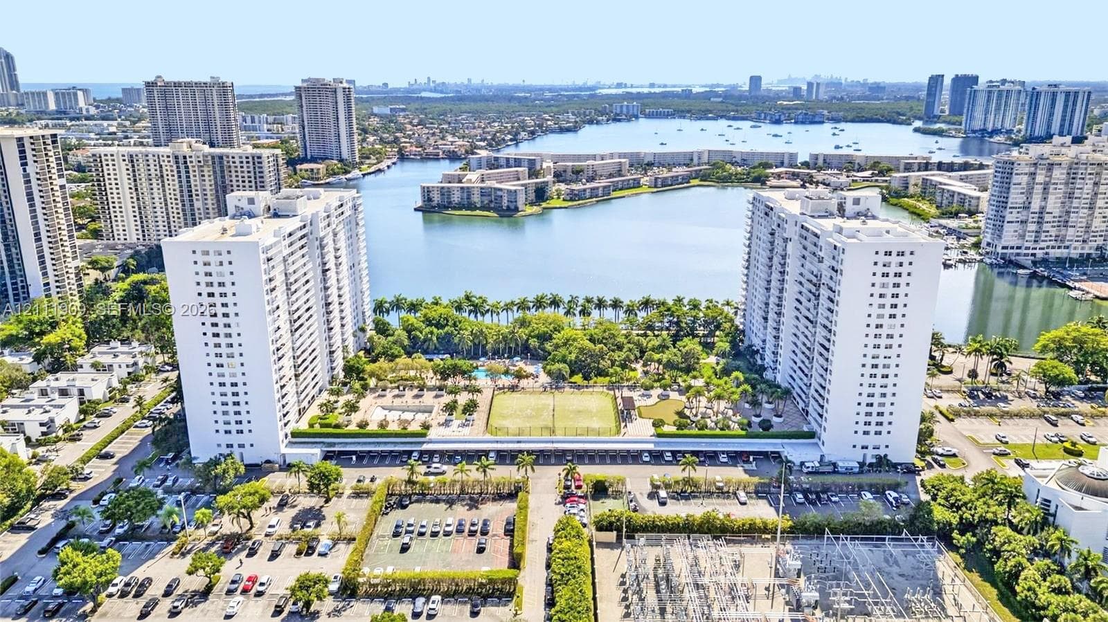 Aerial perspective featuring waterfront high-rise buildings, tennis courts, an outdoor swimming pool, and dedicated parking areas